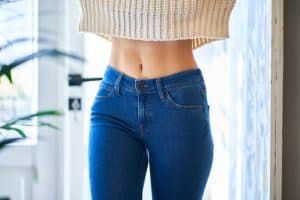 Woman's low cut sweater reveals her belly button, which still looks natural after abdominoplasty.
