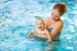 Young mother brings her infant child into a pool for a swim.