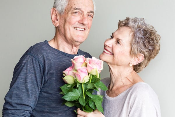 Smiling couple over the age of 60 holds a bouquet of flowers.