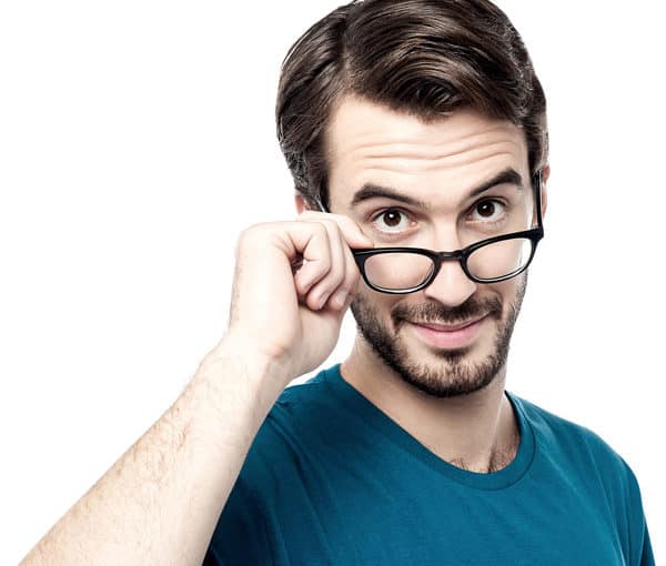 Young male peers over eye glasses with a quizzical expression.
