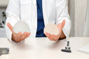 A doctor's hands hold two breast implant sizing options