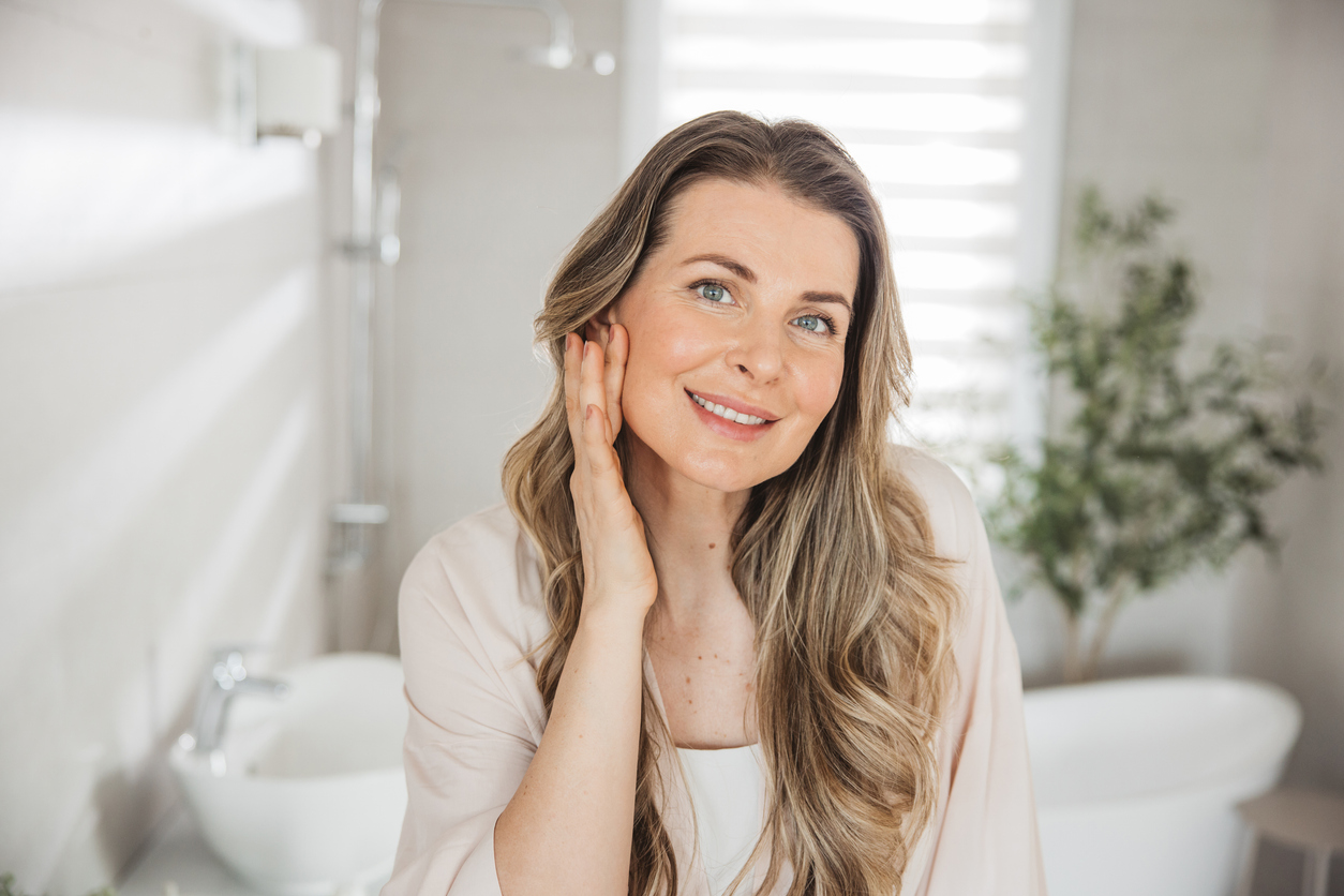 Woman touching her face with her brow and forehead visible in a bright bathroom setting