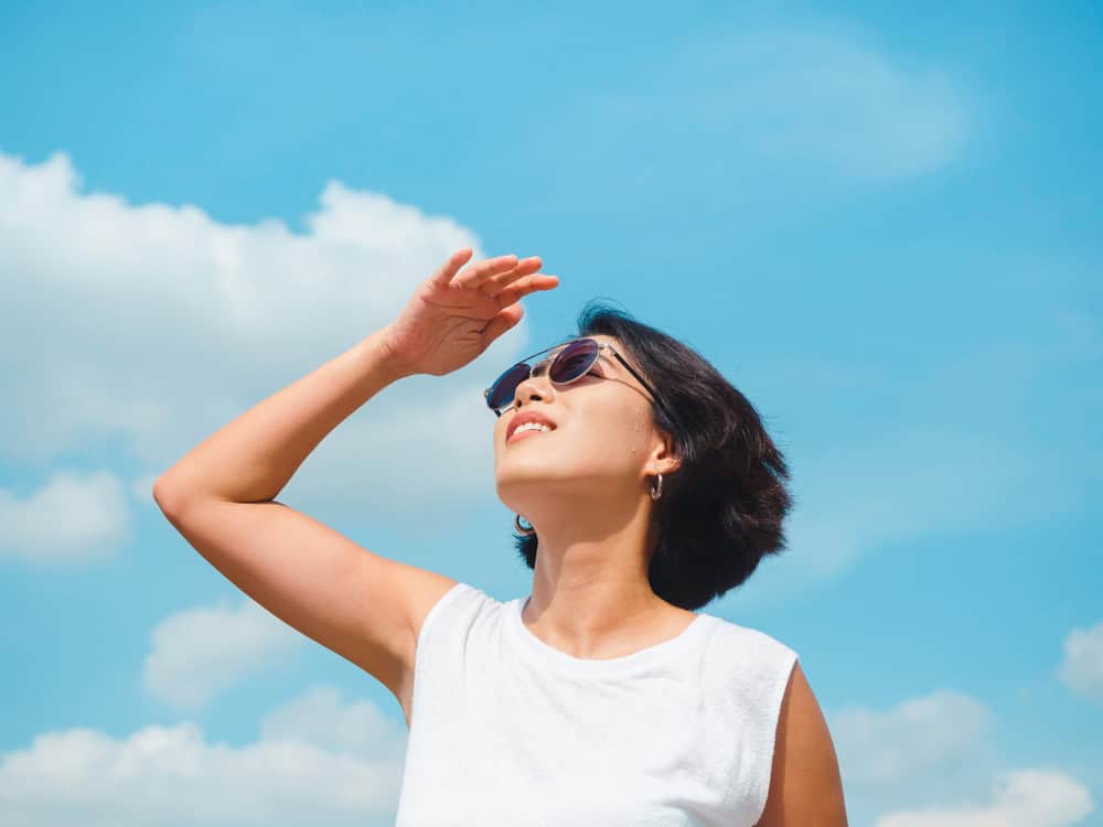 Asian woman with sleek arms in sleeveless shirt looks toward the sky.
