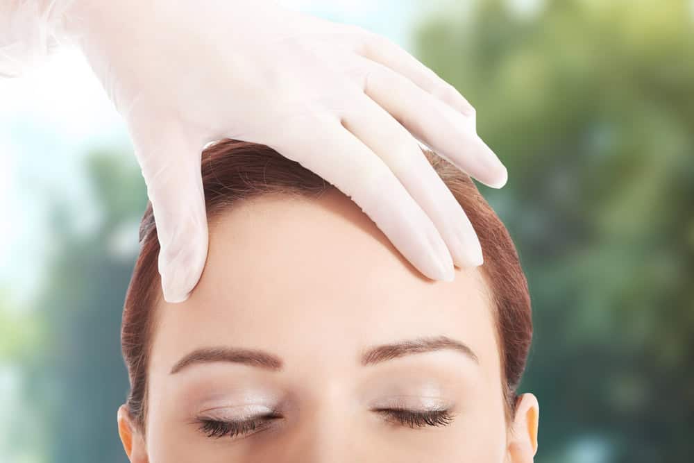 Gloved hand examines women's recovered forehead after brow lift.