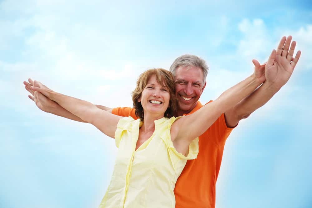 Middle aged woman spreads her arms with her husband standing behind her.