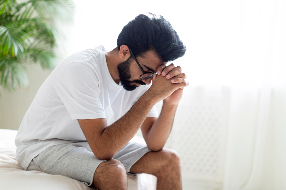 Depressed man with glasses sits on the edge of his bed hoping to try an alternative to antidepressant medication.