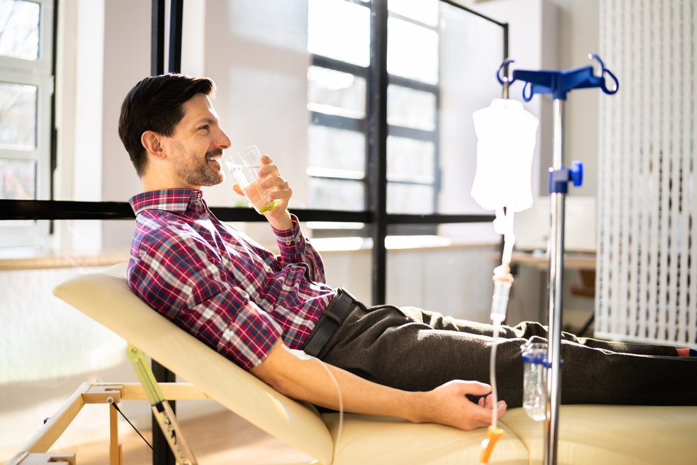 Man enjoys a glass of water during his IV treatment for cellular renewal.