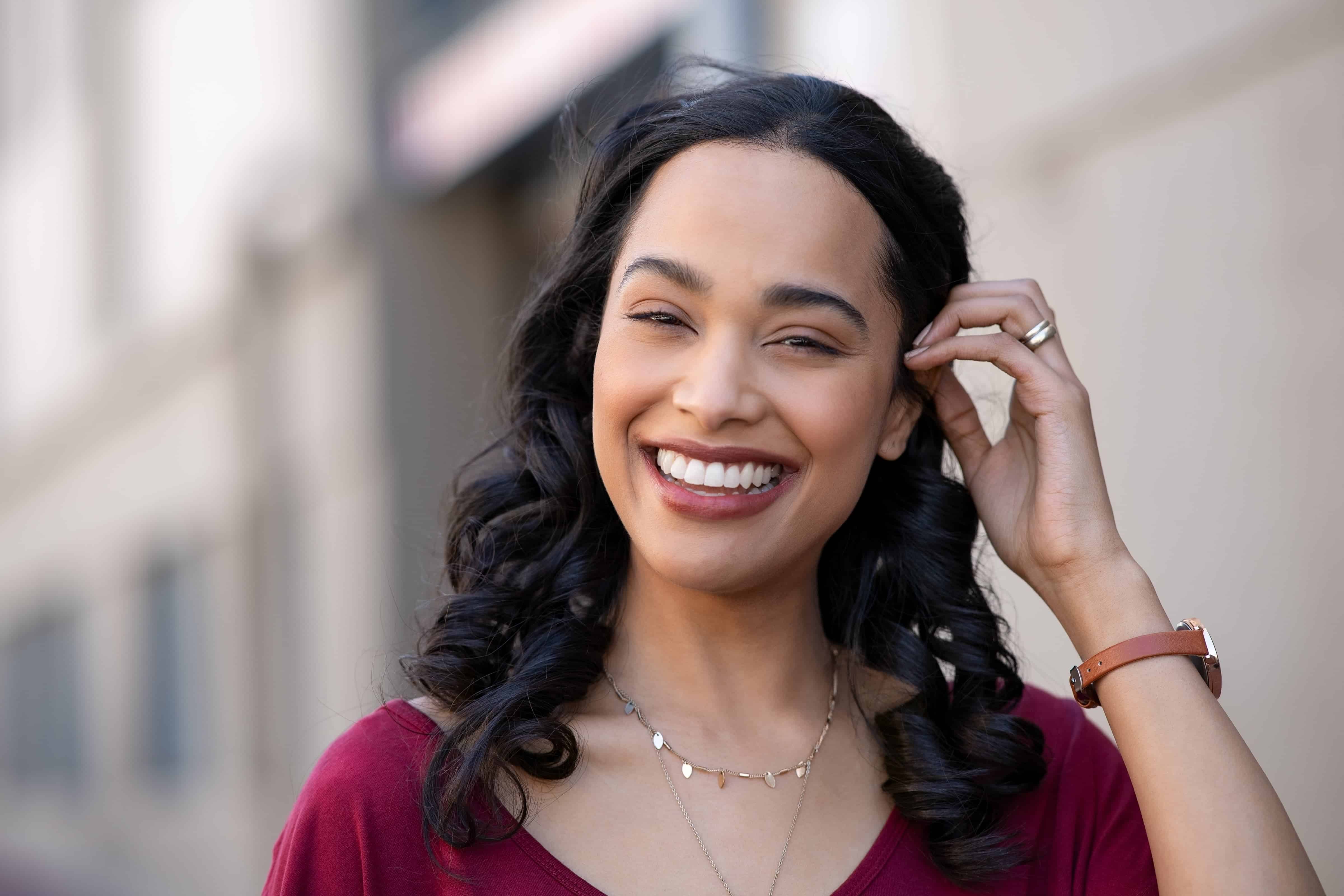 Biracial Latina woman shows beautiful white teeth while walking down a city street