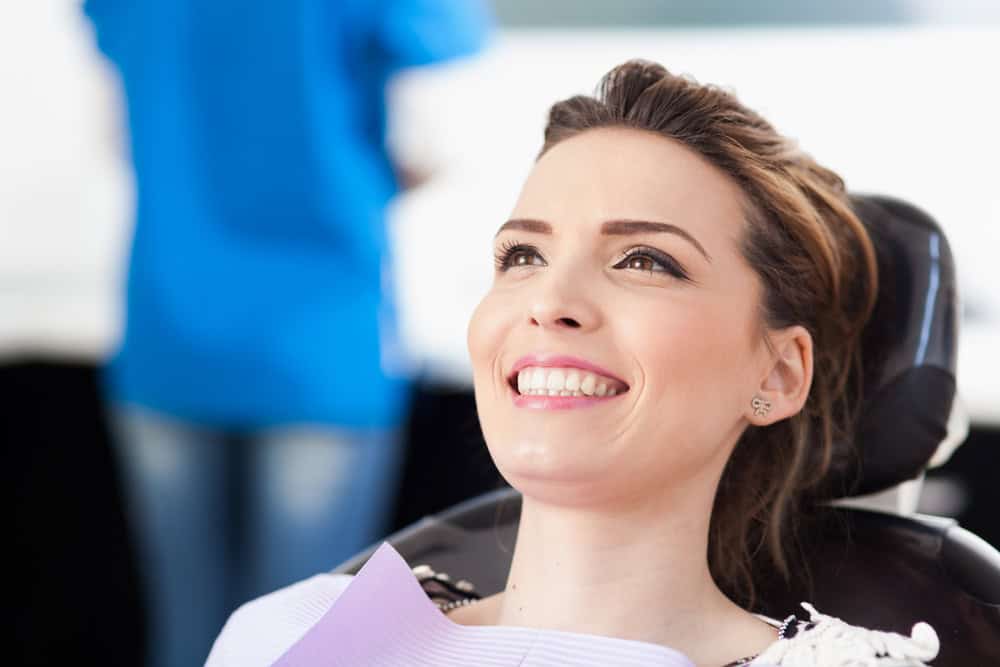 Dental patient relaxes confidently in dental chair, pleased with her beautiful teeth.