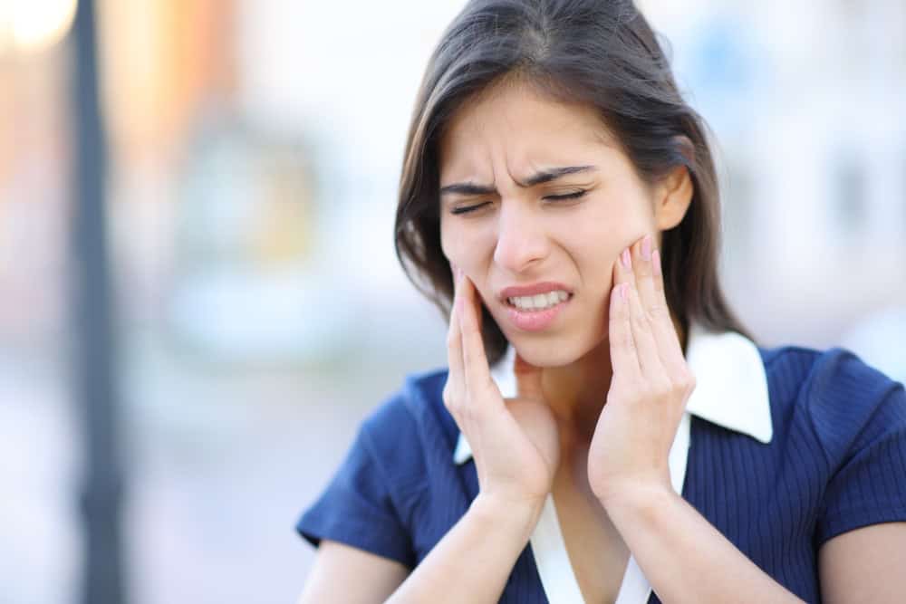 Woman holding her jaw in discomfort from tooth pain or dental sensitivity.