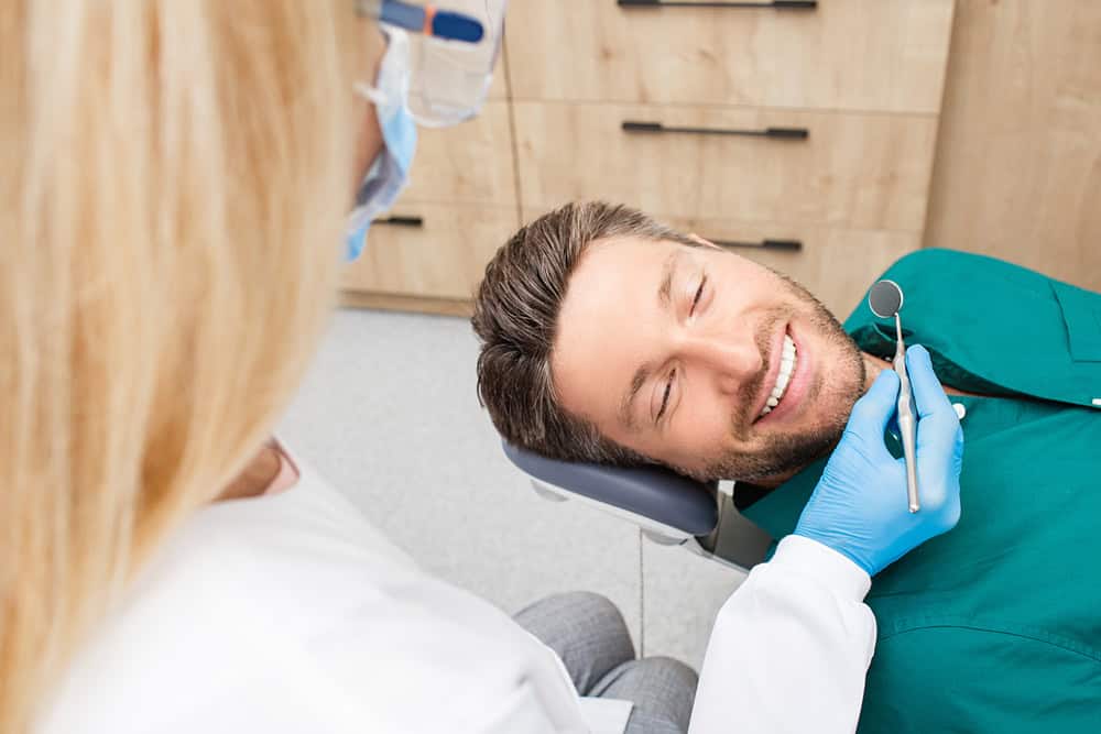 Dentist examining a smiling patient’s teeth during a one-visit dentistry appointment.