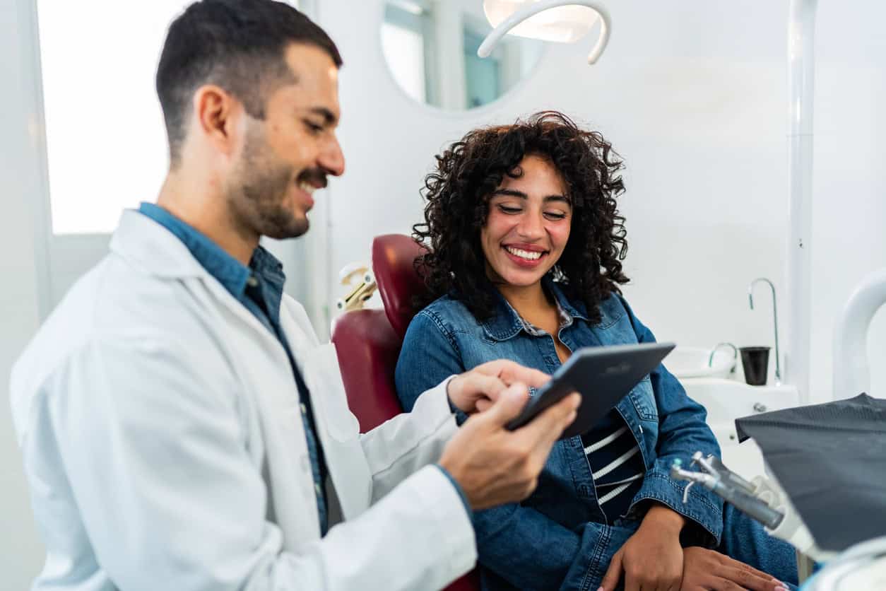 Dentist reviewing treatment details on a tablet with a smiling patient in the exam chair.