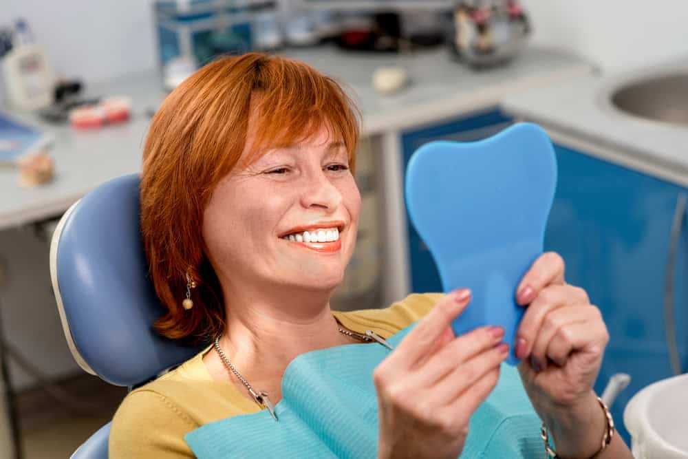 Smiling patient viewing her restored smile in a hand mirror after partial denture treatment.