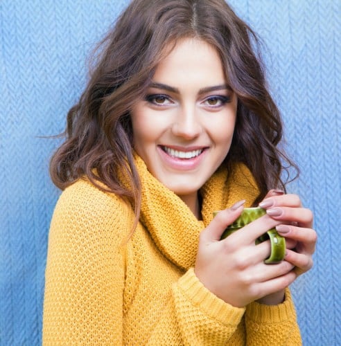 Woman in yellow sweatshirt smiling holding a warm cup of coffee