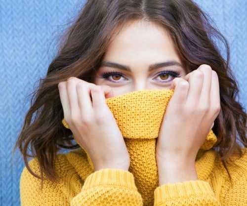 Young woman pulling up her sweater to cover her mouth