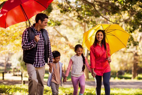 family walking through fall park smiling holding umbrellas