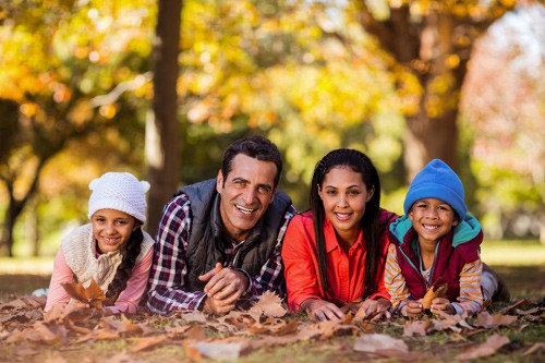 family laying in fall leaves at park smiling