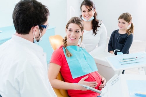 Pregnant woman sitting in dental chair smiling at her doctor