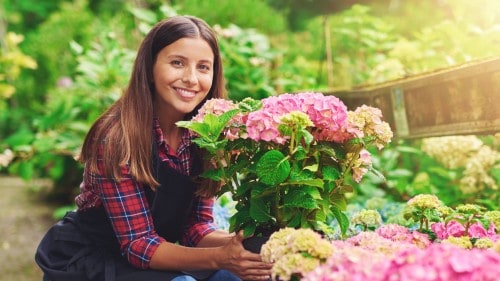 Woman smiling as she plants new flowers in her greenhouse