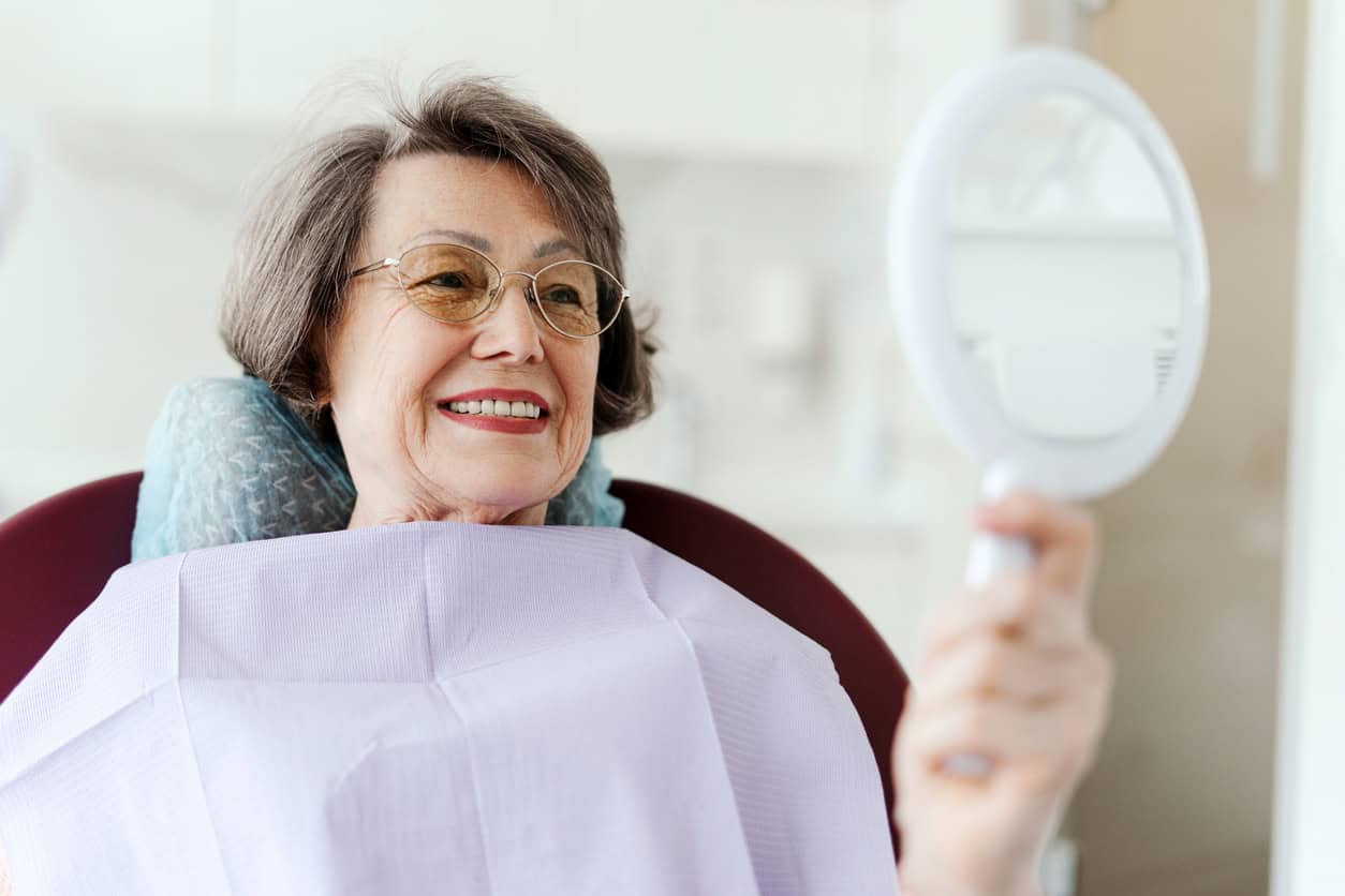 A woman looking in the mirror after receiving full arch dental restorations in Seattle