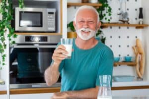 Old man smiles while holding glass of milk. He has great vision.