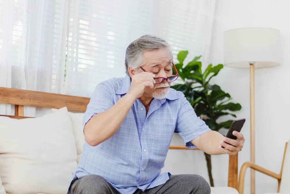Senior man sitting on the couch has trouble making out the text on his phone.