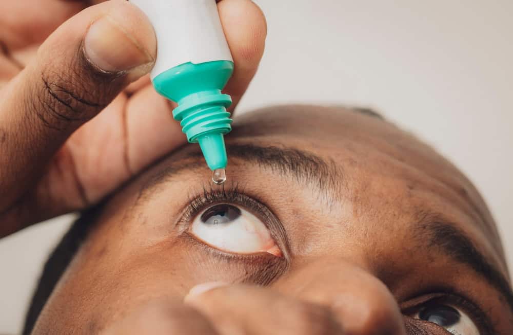 African American man administers eye drops into his eyes affected by glaucoma.