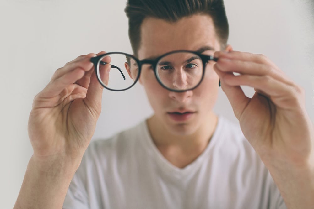 Man holds up glasses unsure whether his prescription for nearsightedness needs changing.